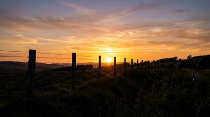 Obraz premium Golden Sunset Glowing Behind Fence Posts in Rural Countryside Field