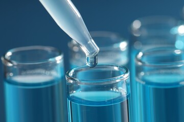 Dripping liquid sample into test tubes with pipette on blue background, closeup © New Africa