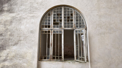 Obraz premium Arched vintage window with broken glass panes in a weathered stone wall
