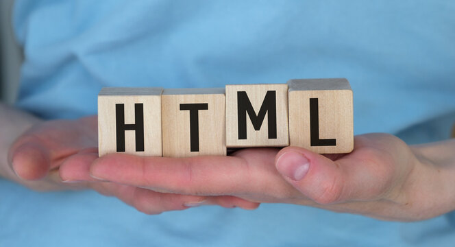Hands hold wooden blocks spelling HTML clearly. Light blue shirt shows soft, professional tone. No facial expression, no emotional cues visible.