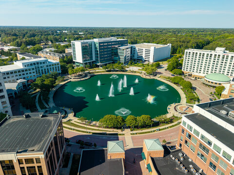 City Center at Oyster Point, Newport News, Virginia, a striking wide-angle aerial drone shot capturing the curved, circular fountain lake, surrounding multi-story commercial offices, and the expansive