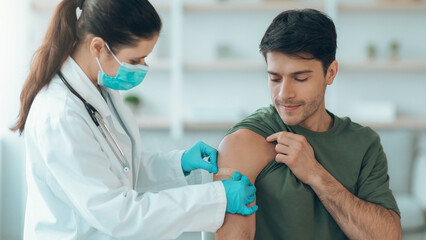 A healthcare worker gives a vaccine to a man in a medical office. The patient sits calmly while...