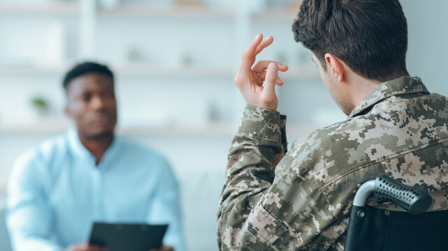 A veteran in a wheelchair talks with a healthcare professional in an office setting. The veteran shares experiences while the professional listens and takes notes on a clipboard.