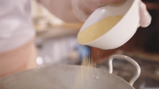 Woman prepares polenta. Rustic kitchen scene with warm natural lighting and cooking process. Woman in cozy traditional kitchen gently pouring yellow cornmeal into hot water
