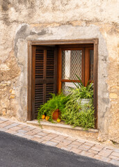 Fototapeta premium Small window with flower pots in brick wall of traditional Mallorca house near street. Mediterranean architecture, rustic detail and cultural heritage.