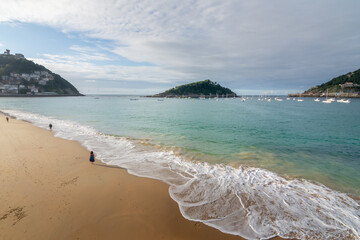 Obraz premium Gentle waves reaching the sandy shore of Ondarreta beach with Santa Clara island in the background in San Sebastian, Spain.