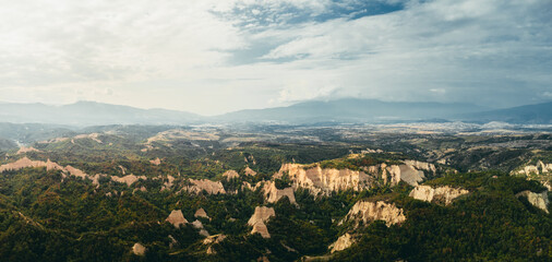 High-resolution aerial landscape of unique sandstone rock formations surrounded by dense green forest and rolling hills. Dramatic natural scenery with textured cliffs, cloudy sky, and untouched wilder © Ibrahim