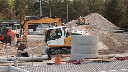 Prace ziemne i montażowe na placu budowy przy użyciu koparki kołowej w pobliżu betonowych elementów kanalizacyjnych. © tomo81