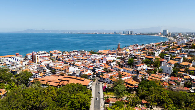 Aerial view of the historic center with red-tiled rooftops and the Parish of Our Lady of Guadalupe overlooking Banderas Bay under a clear blue sky in Puerto Vallarta, Jalisco, Mexico.