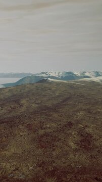 Snow capped mountains rise above a large, rocky landscape. The sky is overcast, and the scene captures the natural features of Icelands terrain during daytime.