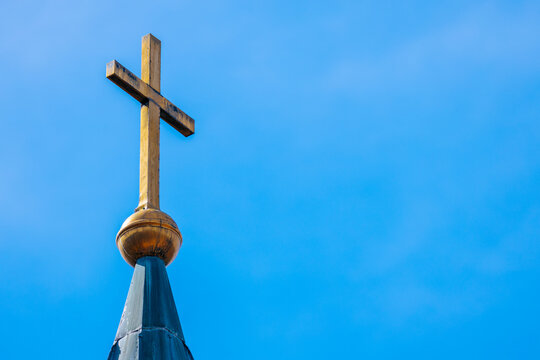 Golden cross atop a church steeple against a clear blue sky, showcasing architectural details and a prominent religious symbol in a serene outdoor setting