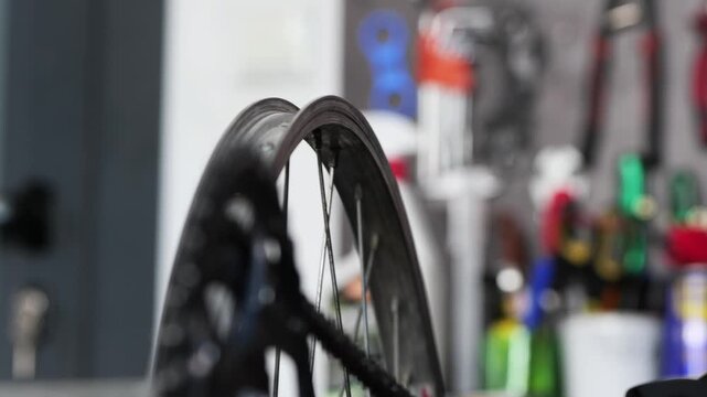 Handheld close up video shows bicycle wheel truing process with hands tightening spokes, rotating rim and moving chain during repair in bike workshop 2026
