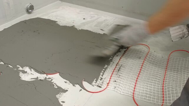 Electric Heating Mat Installing in the Tile Adhesive. Underfloor Dual Core Fiberglass Mesh Mat. Warm Floor Heating System. Warming. Worker Applying Concrete Mortar for Warm Floor. Renovation work. 4K