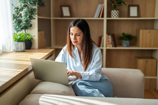 Woman working remotely on laptop from a comfortable home sofa