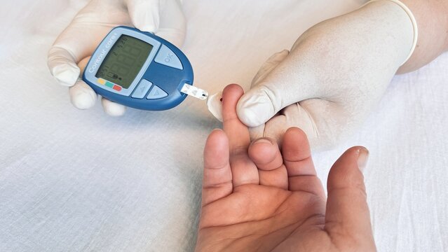 Woman receiving fingerprick blood glucose test from gloved healthcare worker