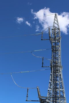 Detailed view of a modern high‑voltage power line tower against a clear blue sky with bright sunlight and scattered cumulus clouds, showcasing contemporary Swedish energy infrastructure.