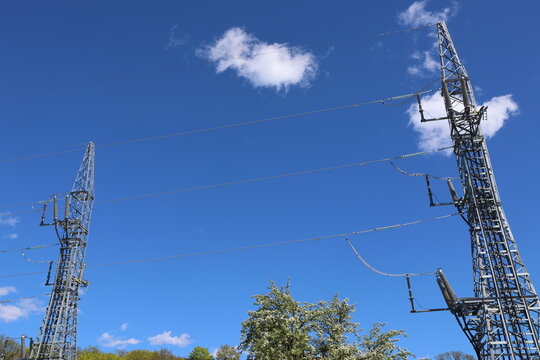 Detailed view of a modern high‑voltage power line tower against a clear blue sky with bright sunlight and scattered cumulus clouds, showcasing contemporary Swedish energy infrastructure.