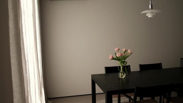 Modern, minimalist dining area and kitchen in a contemporary apartment. Sleek dark wooden dining table set with a glass vase of pink tulips, surrounded by designer chairs