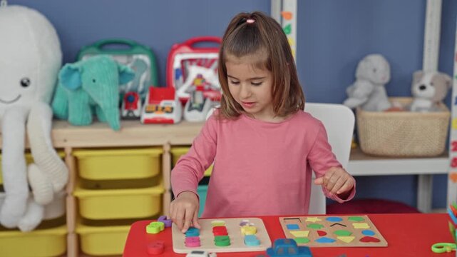 Girl placing wooden shape puzzle piece with right hand on a red play table amid educational toys in a preschool building; learning concentration.