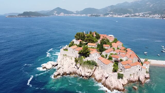 Aerial 4K drone view of Sveti Stefan island, Montenegro, showcasing turquoise waters, lush nature, and stunning coastal scenery