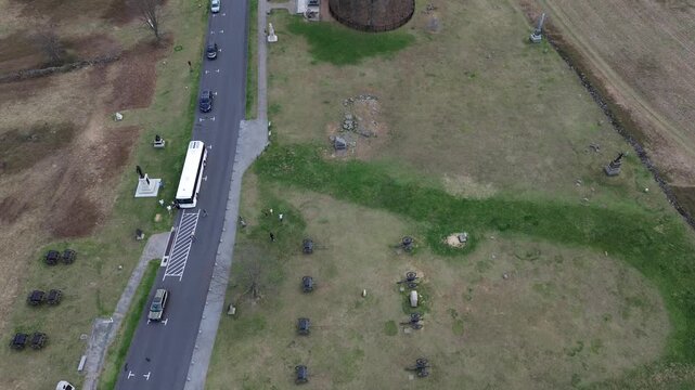 roadside cannon alignment borders Hancock Avenue with parked vehicles, dense monument placements marking Union positions on Gettysburg field. Pale grasses, leafless trees, angled shadows in PA