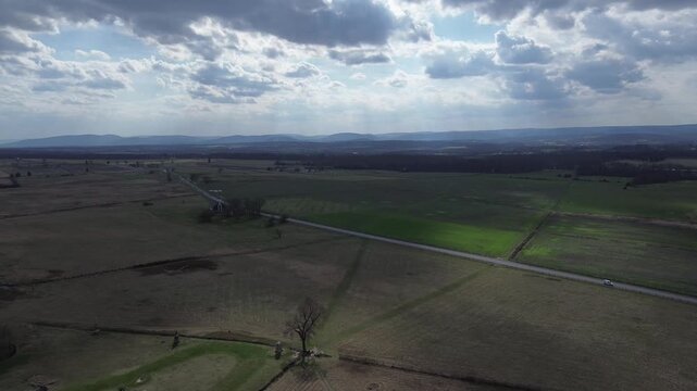Hancock Avenue stretches across Gettysburg NMP with adjacent fenced fields, distant ridge lines defining battlefield&rsquo;s central axis. Mixed winter tones, low sun patches, soft cloud shadows in PA