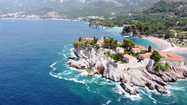 Aerial 4K drone view of Sveti Stefan island from the sea, Montenegro, showcasing turquoise waters and its perfectly preserved historic architecture