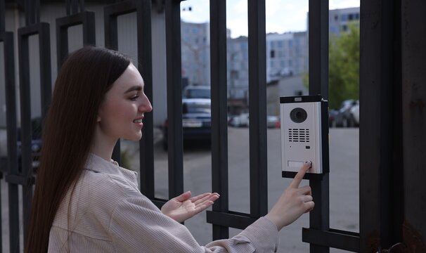 Woman pressing button on intercom panel outdoors
