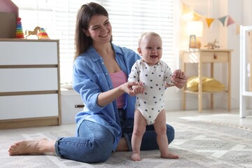Obraz premium First steps. Mother supporting daughter while she learning to walk at home