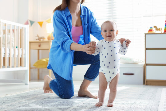 First steps. Mother supporting daughter while she learning to walk at home, closeup
