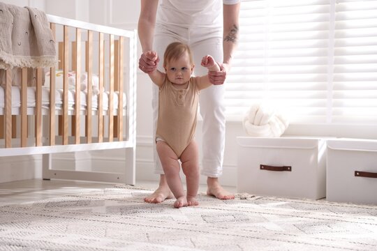 Baby's first steps. Mother supporting daughter while she learning to walk at home, closeup