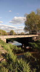 Mały most betonowy nad spokojną rzeką w sielskim, zielonym krajobrazie pod błękitnym niebem z chmurami. © tomo81