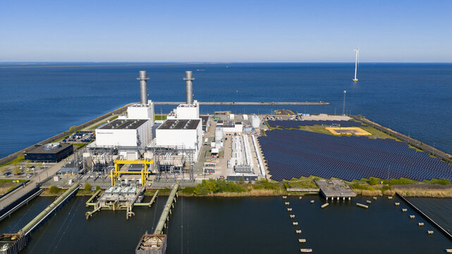 Aerial view of the ENGIE Maxima plant with solar panels, industrial buildings, and a wind turbine on the coast of Lelystad, Flevoland, Netherlands.