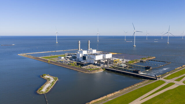 Aerial view of the Maxima power plant with industrial buildings and smokestacks surrounded by water and offshore wind turbines in Lelystad, Flevoland, Netherlands.