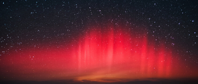 Vibrant red aurora borealis illuminates a starry night sky over dark horizon