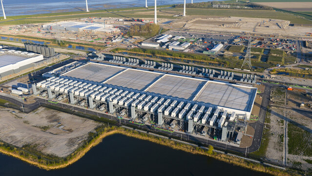 Aerial view of the Google GRQ data center facility with rows of cooling units, construction sites, and wind turbines in Eemshaven, Groningen, Netherlands.