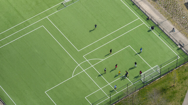 Aerial view of people playing football on a green artificial turf pitch with white markings and goal posts in Amsterdam, Noord-Holland, Netherlands.