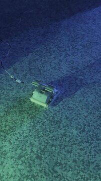 Robotic pool cleaner moving along mosaic tile floor of swimming pool underwater with blue green illumination during automatic pool maintenance. High quality 4k footage