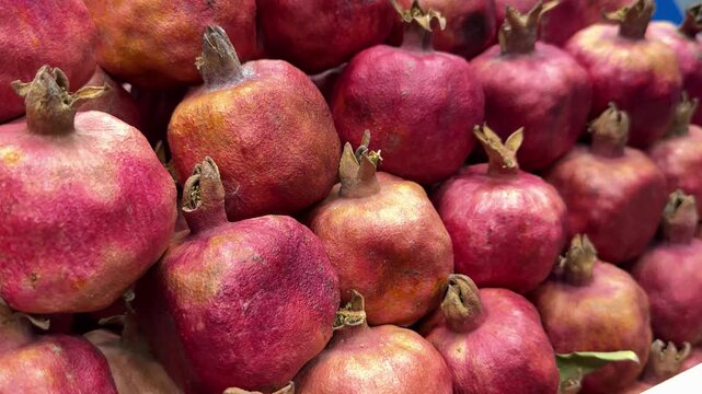 Ripe pomegranate fruits piled together, vibrant close-up of red skins and dried crowns, market stall arrangement with rustic