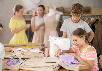 Girl sews on a sewing machine. A boy watches and learns © JackF