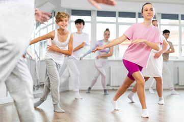 Fototapeta premium Team of positive teenagers rehearsing modern dances in dance hall