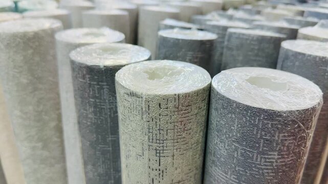 Close-up wallpaper rolls in showroom, soft muted teal gray beige textures, vertical rolls lined on shelf, embossed grain patterns