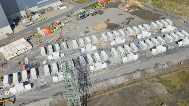 Aerial view of the RWE Westfalen power plant featuring rows of battery storage containers and an electricity pylon under bright daylight in Hamm, Nordrhein-Westfalen, Germany.