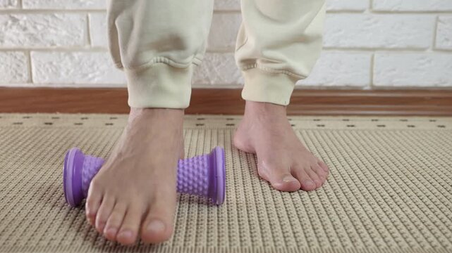 Woman doing foot massage using a roller. Close-up of a woman's feet massaging on a purple spiky roller to relieve pain from plantar fasciitis, providing muscle relaxation and physical therapy
