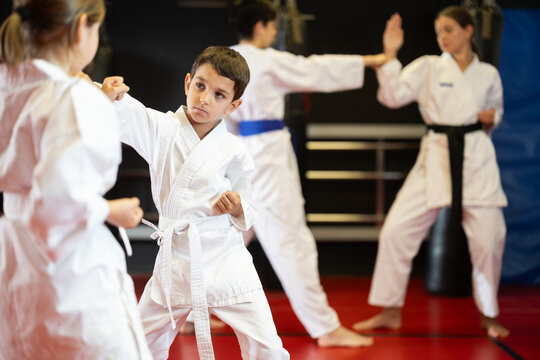 Boy and girl in kimonos train karate techniques in group in studio