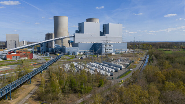 Aerial view of the RWE Westfalen power plant with cooling towers and industrial structures surrounded by green trees under a clear blue sky in Hamm, Nordrhein-Westfalen, Germany.