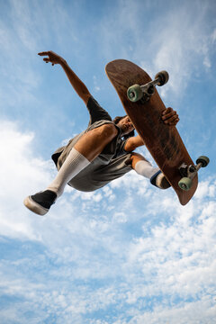 Skateboarder jumping mid-air with board against blue sky
