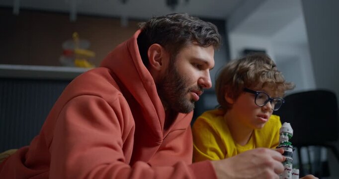 Father and young son collaborating at home on a small rocket model, sharing a focused family learning moment during a hands-on creative project