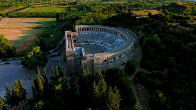 Drone view of Aspendos Theatre entrance. Historic amphitheater walls and stage building stand among green trees in Antalya.