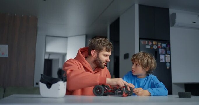 Father and young son assembling a small remote controlled car at a kitchen table, sharing focused hands-on learning in a modern home interior